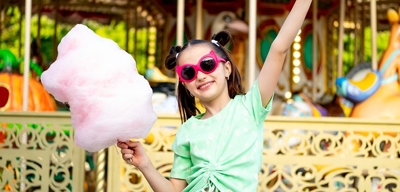 Smiling girl holding pink cotton candy in front of a carousel Smiling girl holding pink cotton candy in front of a carousel